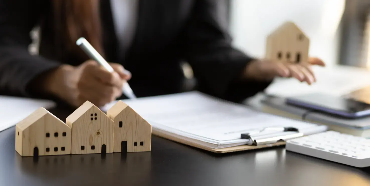 Person handling real estate paperwork with wooden house models, representing a contingent home sale