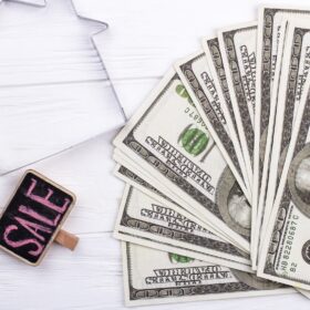 Outline of a house with a 'For Sale' sign and stacks of hundred dollar bills on a table, representing tips for selling a house for cash.