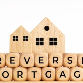 Wooden blocks spelling 'reverse mortgage' with two wooden houses on top, symbolizing selling a house with a reverse mortgage.