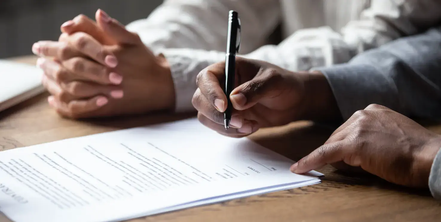 People reviewing and signing paperwork, representing selling a house in a trust before death