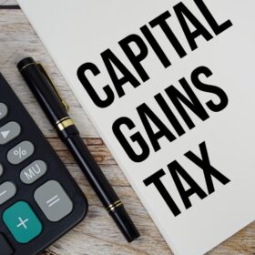 Calculator and folder labeled 'Capital Gains Tax' on a table, symbolizing the calculation of capital gains taxes on a rental property.