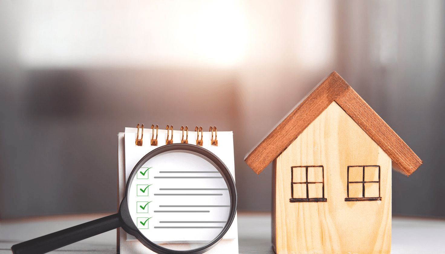 Magnifying glass over a checklist next to a wooden house model, symbolizing a pre-listing home inspection.